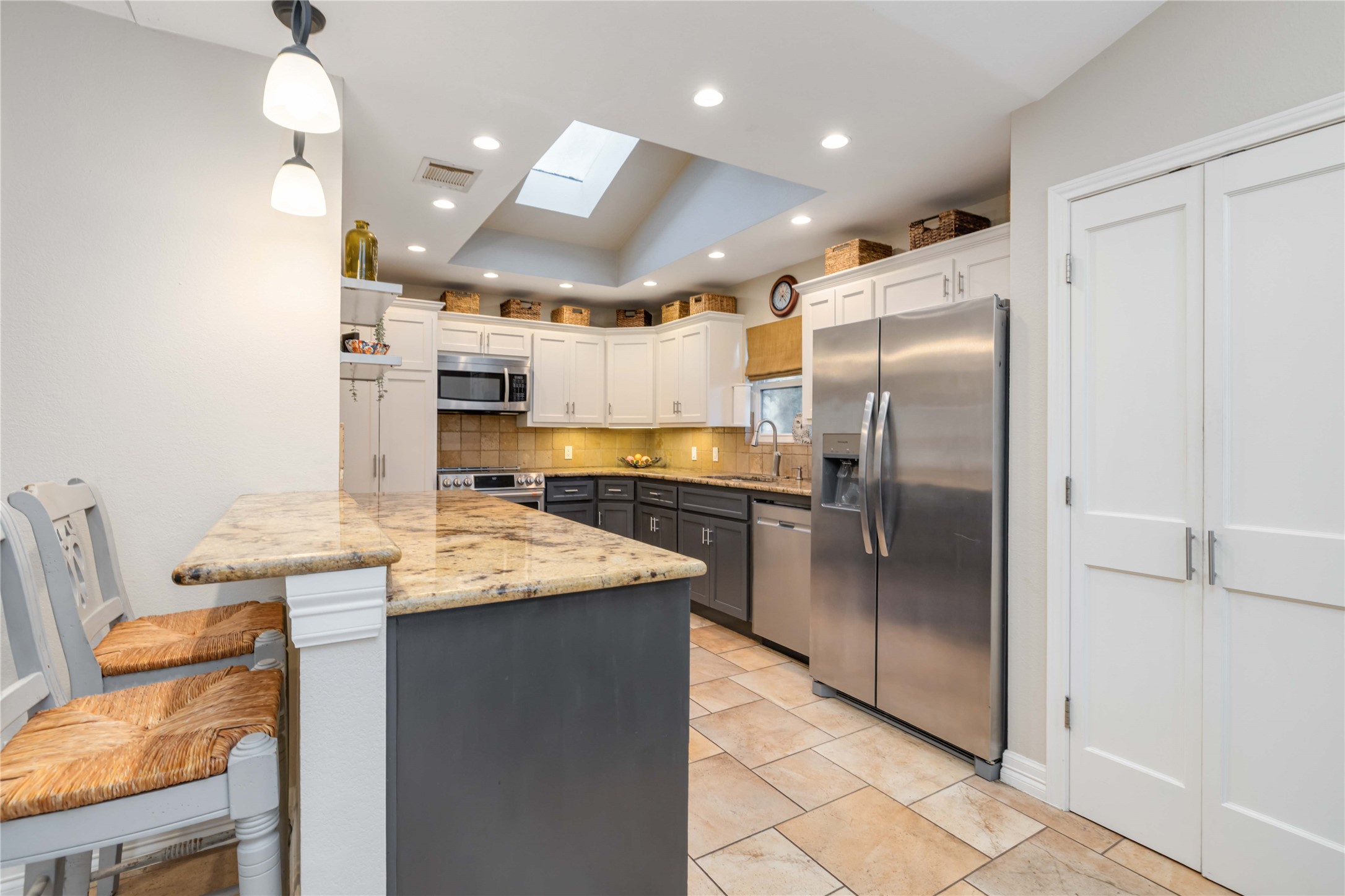 10903 Cade Circle Austin, TX 78726 - Photo 21 of 40 Two tone kitchen with dual tone cabinets, stainless steel appliances, tasteful backsplash, decorative light fixtures, and a skylight