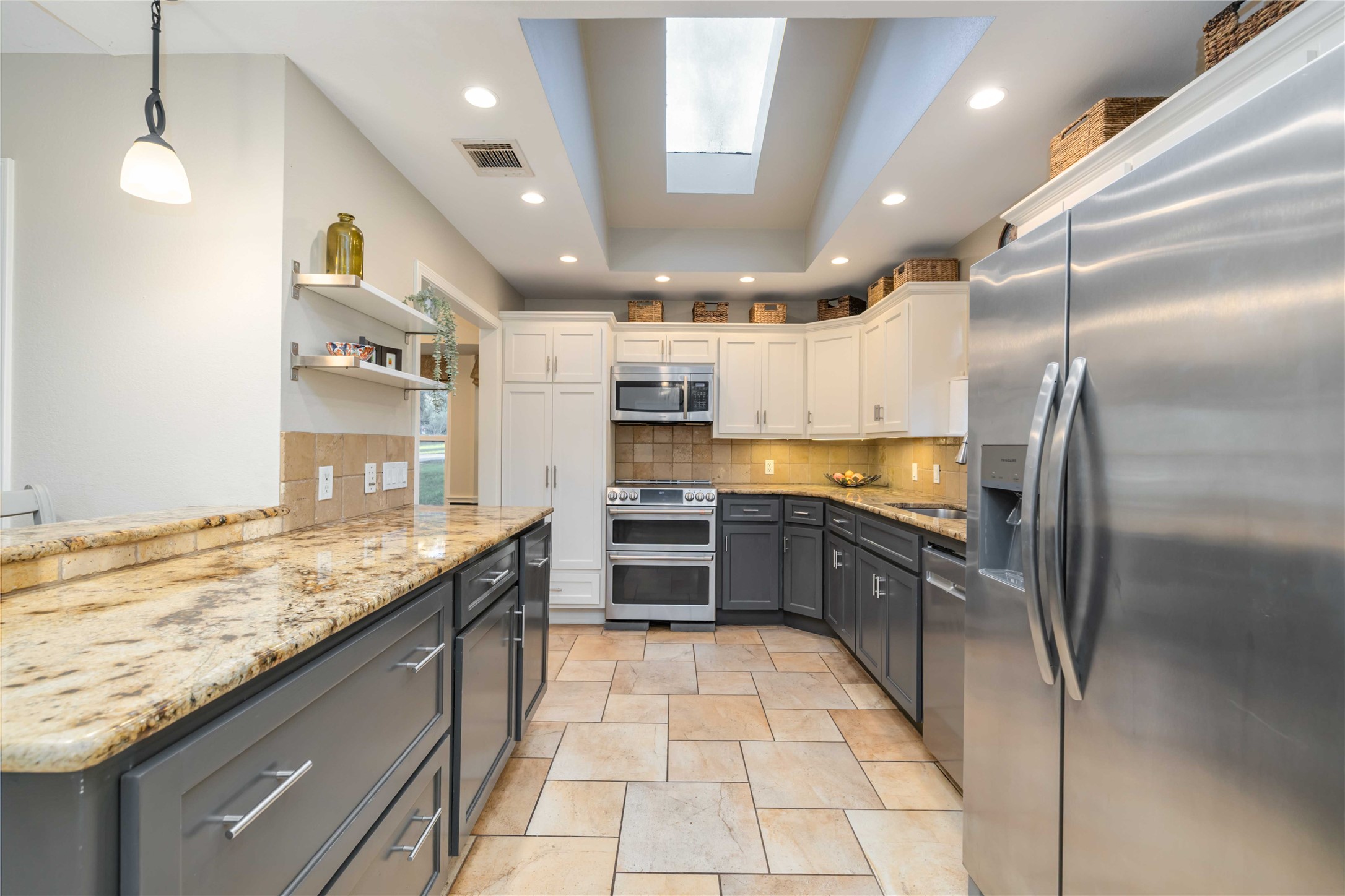 10903 Cade Circle Austin, TX 78726 - Photo 22 of 40 Kitchen featuring two tone cabinetry, stainless steel appliances, light stone counters, a skylight, and decorative light fixtures