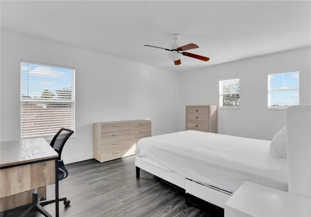 a bedroom with a bed a desk and chair with wooden floor