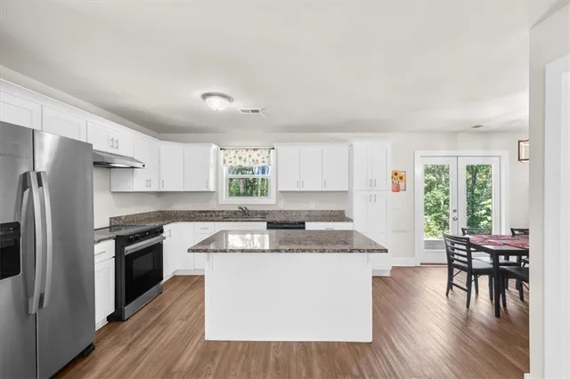 a kitchen with granite countertop a stove top oven a sink dishwasher a dining table and chairs with wooden floor