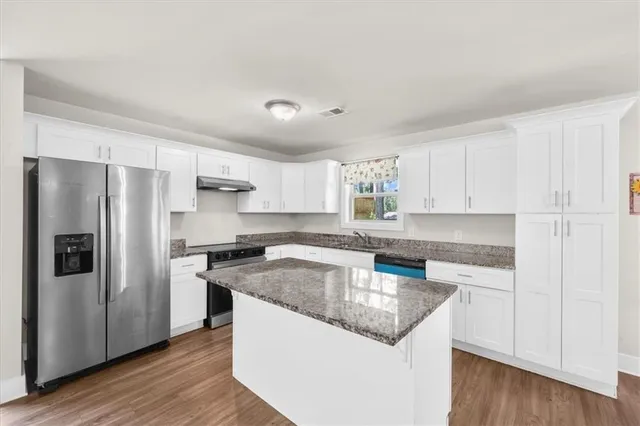a kitchen with granite countertop stainless steel appliances a refrigerator a sink and cabinets