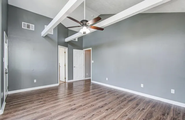 a view of an empty room with wooden floor and a ceiling fan