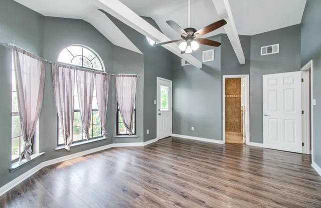an empty room with wooden floor fan and windows