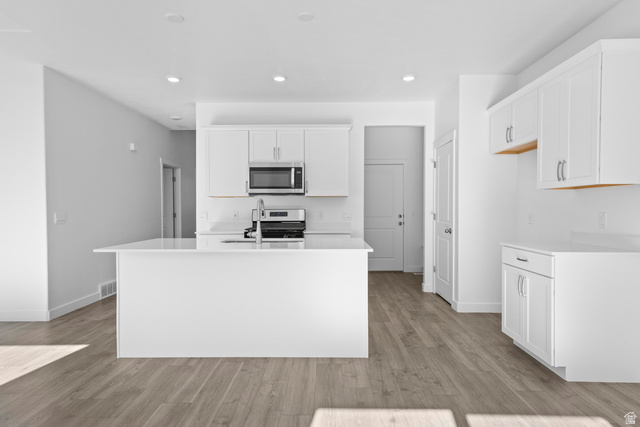 2823 North 710 West, Unit 16 Logan, UT 84321 - Photo 18 of 22 Kitchen with white cabinetry, light wood-style flooring, a center island with sink, stainless steel appliances, and light stone counters