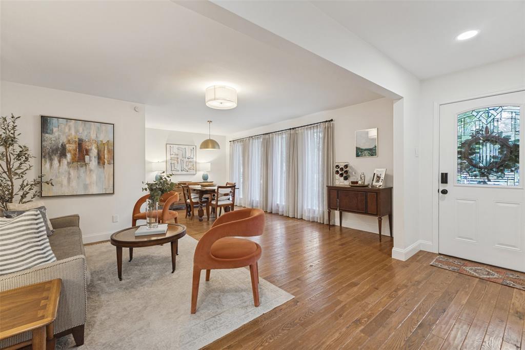 Light-filled living space with wood-finish flooring, a white paneled entry door with leaded glass, and a dining area