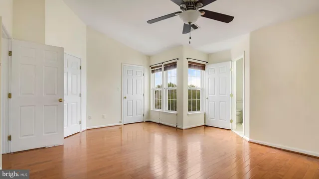 a view of an empty room with wooden floor and a ceiling fan