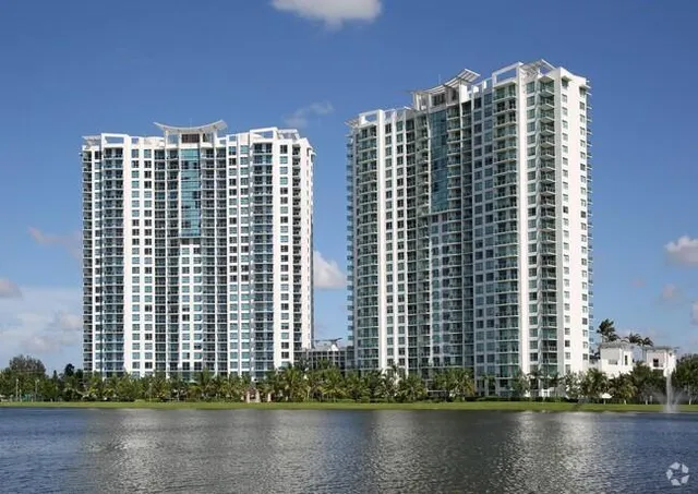 a front view of a building with lake view and tall trees