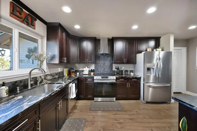 a kitchen with stainless steel appliances granite countertop a refrigerator a stove and a wooden floors