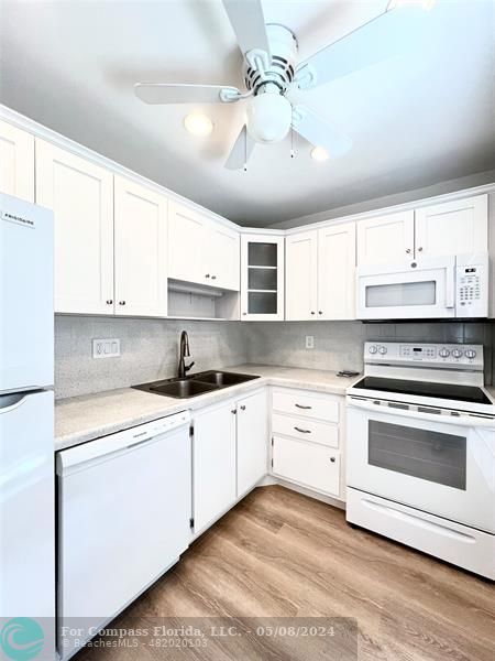 a kitchen with stainless steel appliances granite countertop a sink dishwasher a stove and white cabinets with wooden floor