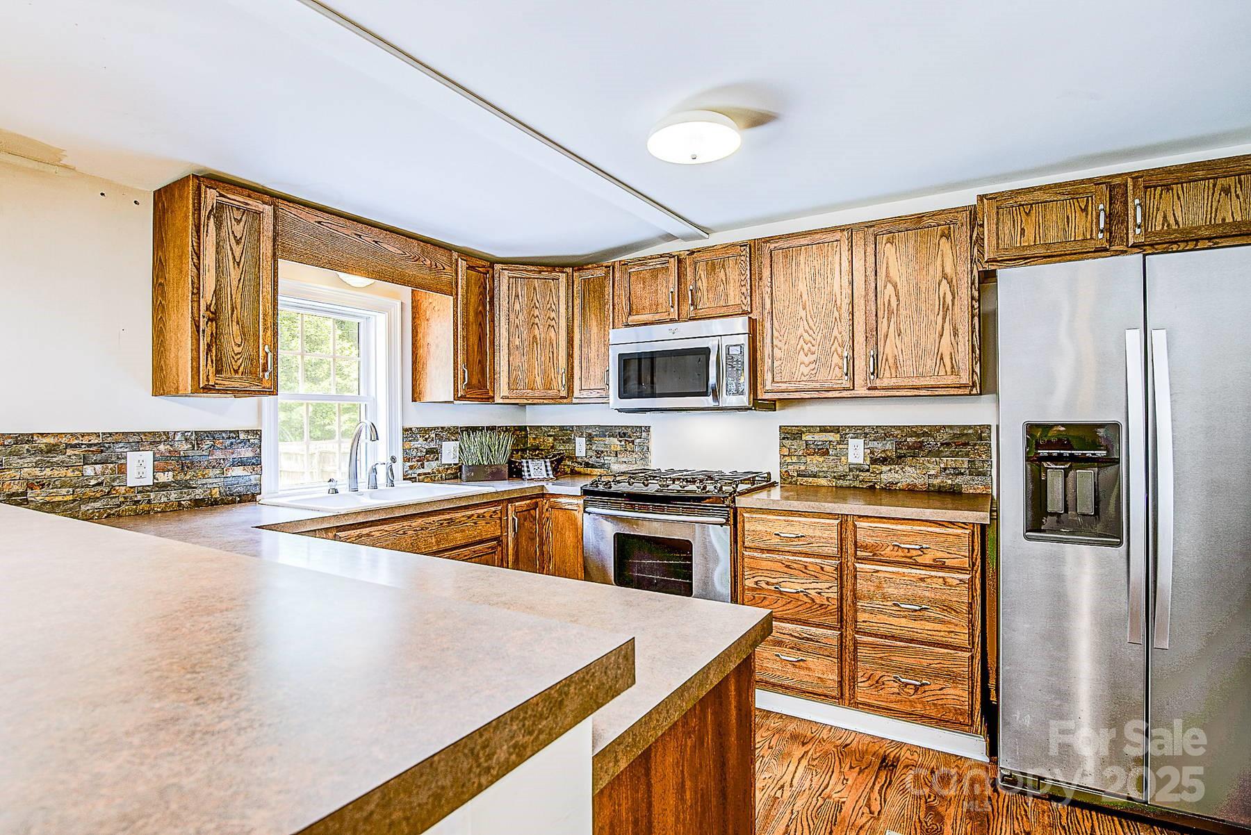 5165 Woodleaf Road Salisbury, NC 28147 - Photo 13 of 48 a kitchen with stainless steel appliances granite countertop a refrigerator a stove top oven a sink dishwasher and white cabinets with wooden floor
