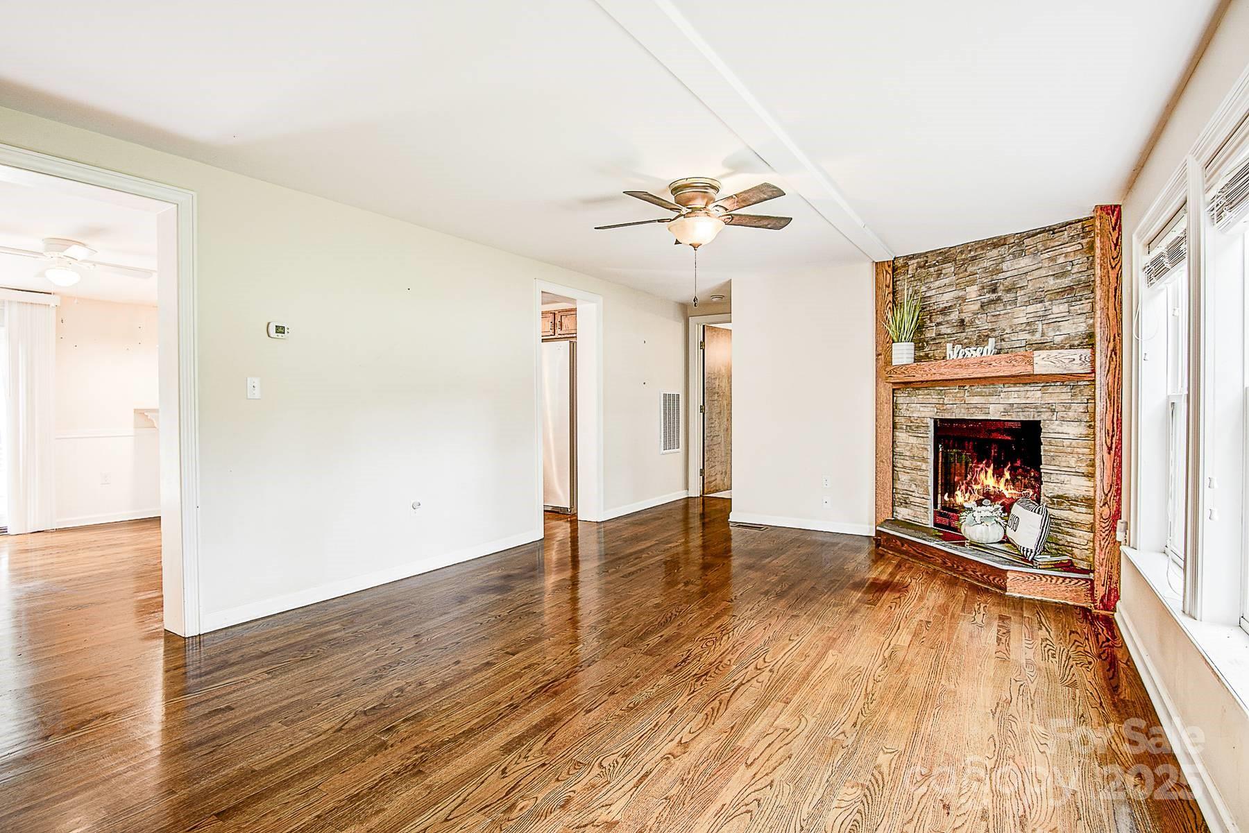 5165 Woodleaf Road Salisbury, NC 28147 - Photo 6 of 48 an empty room with wooden floor a fireplace a ceiling fan and windows