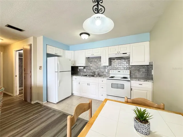 a kitchen with stainless steel appliances granite countertop a refrigerator a stove and white cabinets with wooden floor