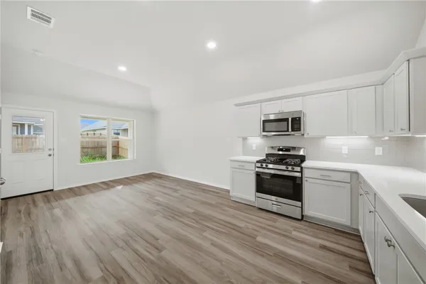 a kitchen with stainless steel appliances granite countertop a stove top oven a sink dishwasher and a refrigerator with wooden floor