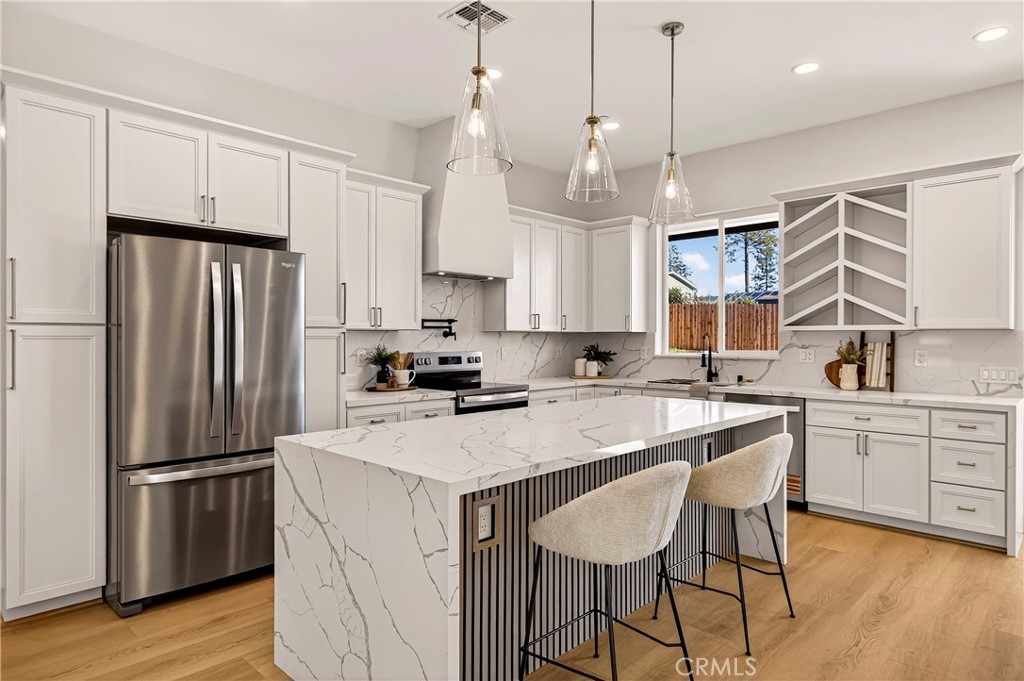 a kitchen with stainless steel appliances granite countertop a refrigerator a sink dishwasher a stove and white cabinets with wooden floor