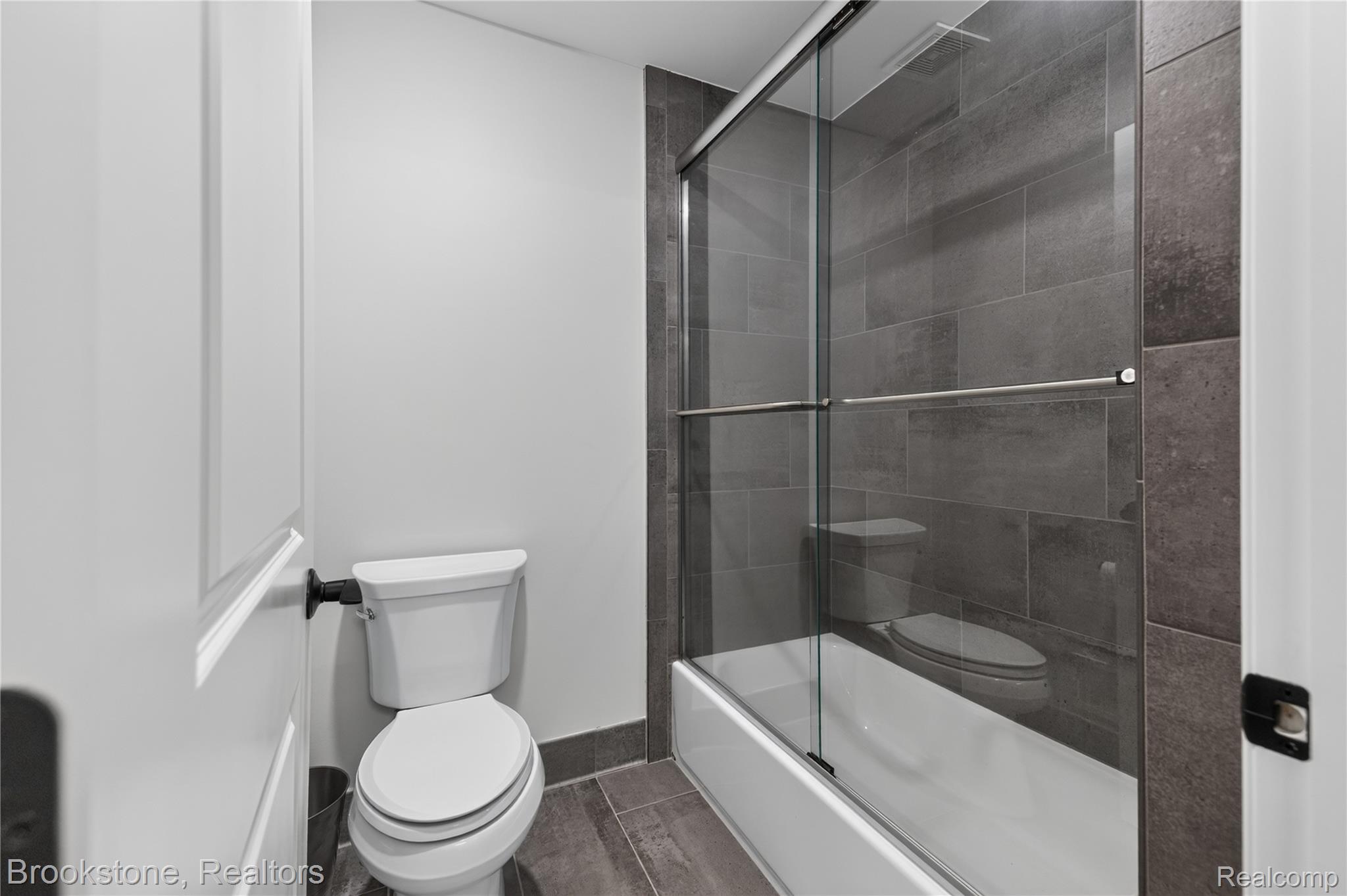 2167 Sanctuary Court Rochester, MI 48309 - Photo 22 of 68 Bathroom featuring a full-size bathtub with a glass sliding enclosure, dark gray tile surround, and coordinating tile flooring