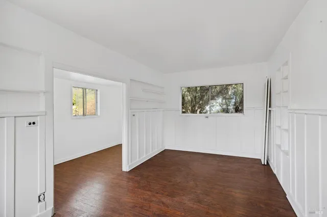 an empty room with wooden floor closet and windows