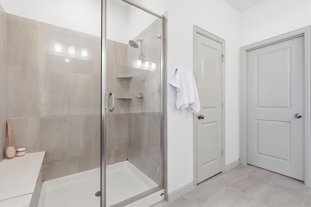 6141 Roper Road McKinney, TX 75070 - Photo 20 of 35 Glass-enclosed shower featuring light-toned large format tile, a built-in bench, and an integrated showerhead