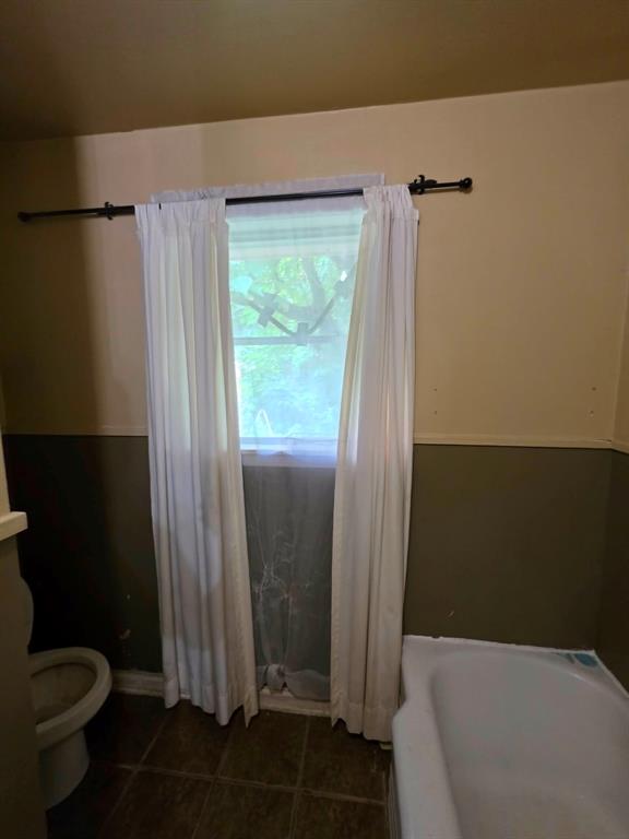4514 West Loop 281 Longview, TX 75604 - Photo 29 of 36 Bathroom featuring a window with white curtains, a white bathtub, a toilet, and dark tile flooring