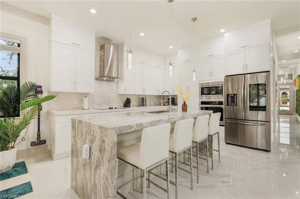 614 105th Avenue North Naples, FL 34108 - Photo 7 of 37 a kitchen with stainless steel appliances kitchen island granite countertop a refrigerator a stove a sink a dining table and chairs with wooden floor