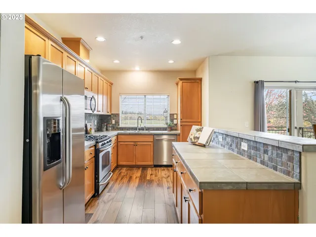 a kitchen with stainless steel appliances granite countertop a refrigerator a sink dishwasher and a stove with wooden floor