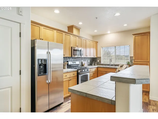 a kitchen with stainless steel appliances kitchen island granite countertop a refrigerator a stove and a sink with wooden floor