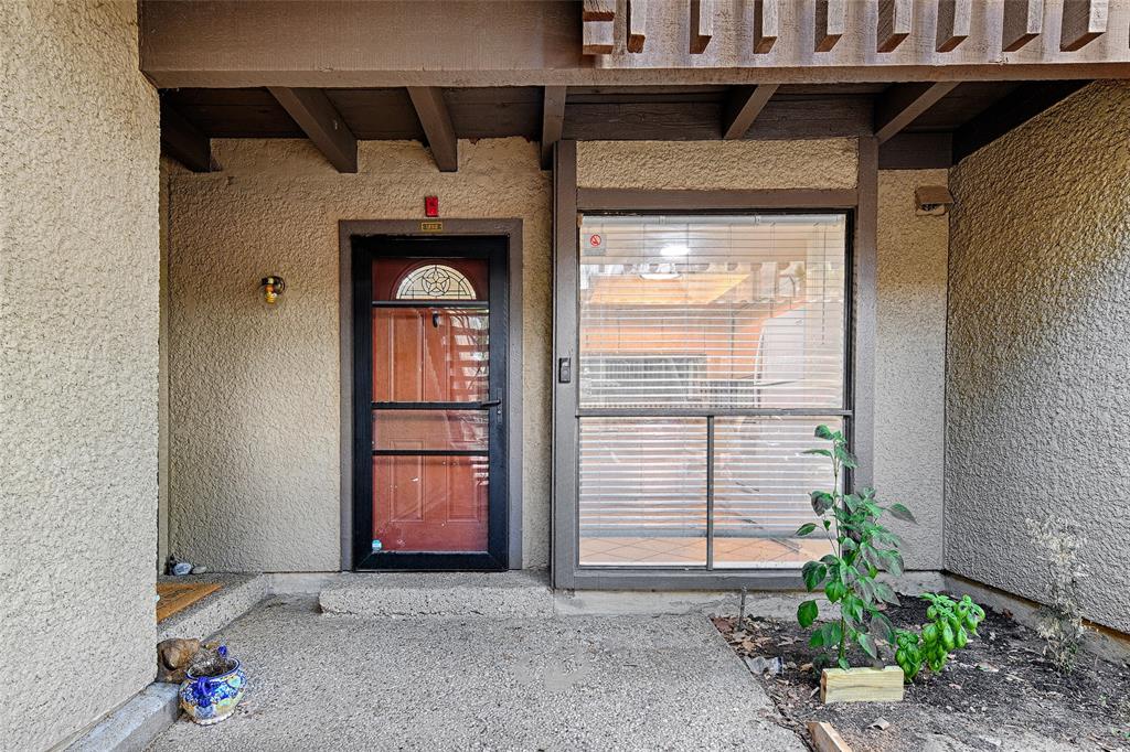 4561 North O'Connor Road, Unit 1292 Irving, TX 75062 - Photo 2 of 10 Entryway featuring a red paneled door with a decorative arch window, a storm door, textured stucco siding, an exposed beam ceiling, and a concrete patio