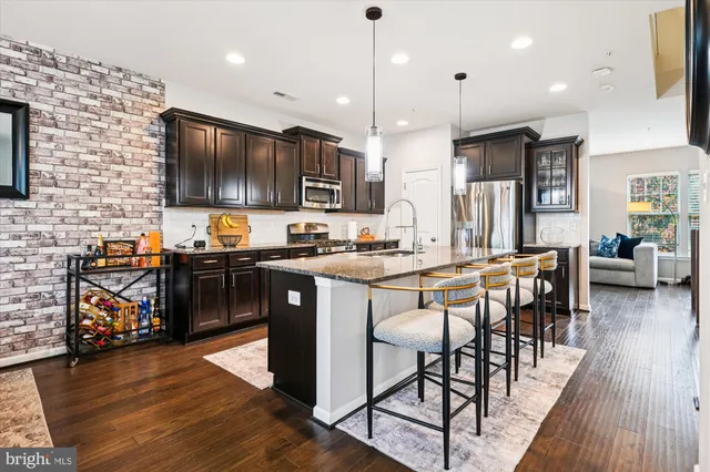a kitchen with stainless steel appliances kitchen island granite countertop a refrigerator a stove a sink a dining table and chairs with wooden floor