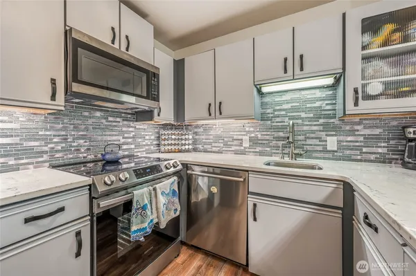 a kitchen with stainless steel appliances granite countertop a stove top oven a sink dishwasher and white cabinets with wooden floor