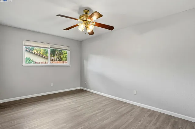 an empty room with wooden floor chandelier fan and windows