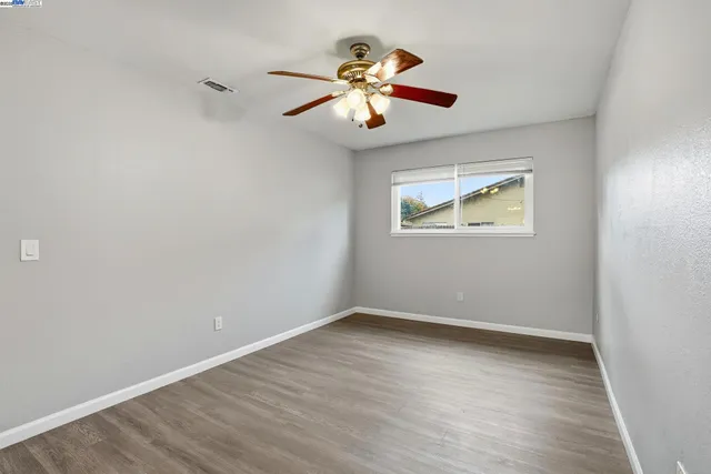 an empty room with wooden floor chandelier fan and windows