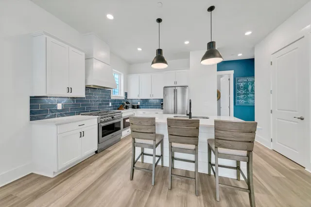 a kitchen with stainless steel appliances kitchen island granite countertop a dining table chairs stove and white cabinets