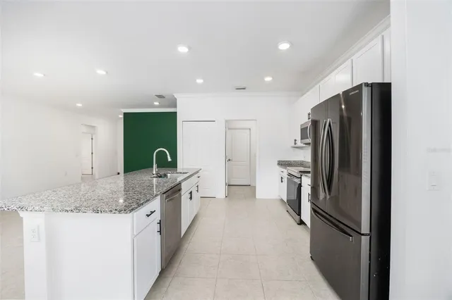 a kitchen with stainless steel appliances granite countertop a stove a refrigerator a sink and white cabinets