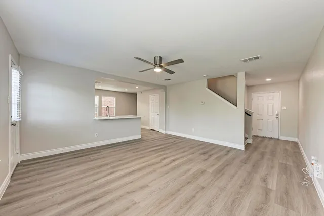 an empty room with wooden floor a ceiling fan and windows
