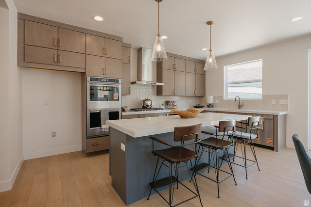 5902 Canyon Rim Road, Unit 620 Lehi, UT 84048 - Photo 7 of 78 Contemporary kitchen featuring light wood-finish flooring, an expansive island with a light-toned countertop, stainless steel appliances including a built-in double oven, and recessed lighting with pendant fixtures