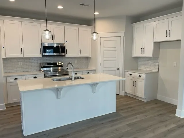 a kitchen with stainless steel appliances granite countertop a sink a stove a refrigerator and white cabinets