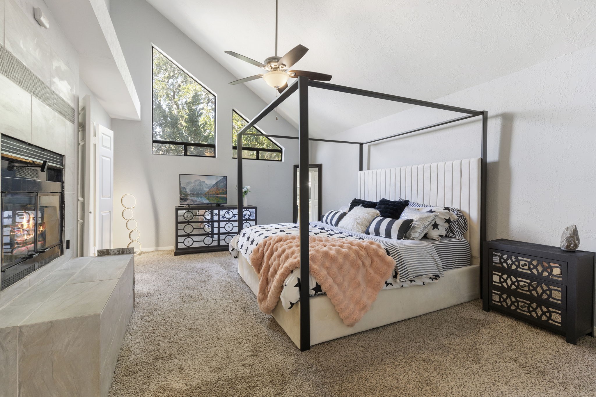 2110 Paso Rello Drive Houston, TX 77077 - Photo 25 of 41 A spacious bedroom featuring a cozy fireplace, high vaulted ceilings, and large windows that let in plenty of natural light. The room includes a stylish four-poster bed, plush carpet, and modern decor, creating a warm and inviting atmosphere.