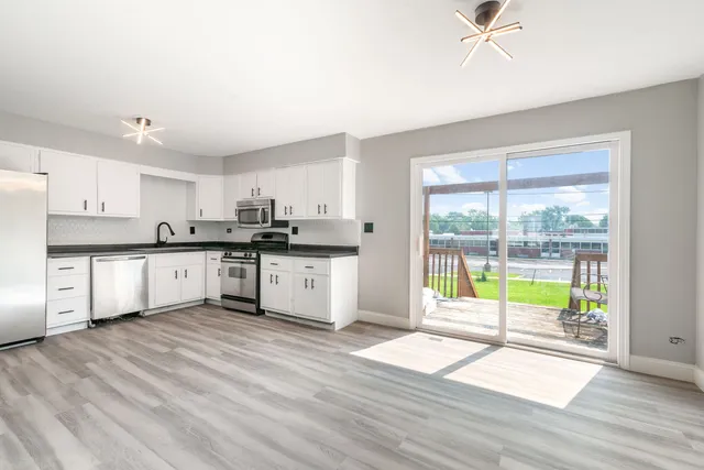 a kitchen with stainless steel appliances granite countertop a refrigerator a sink a stove and white cabinets with wooden floor