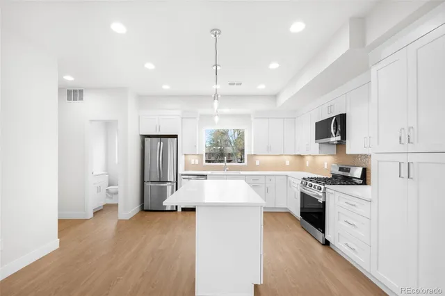 a kitchen with stainless steel appliances granite countertop a refrigerator a stove oven a sink dishwasher and white cabinets with wooden floor