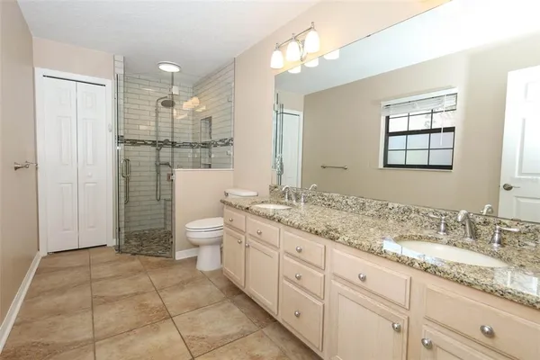 a bathroom with a granite countertop sink a toilet a mirror and shower