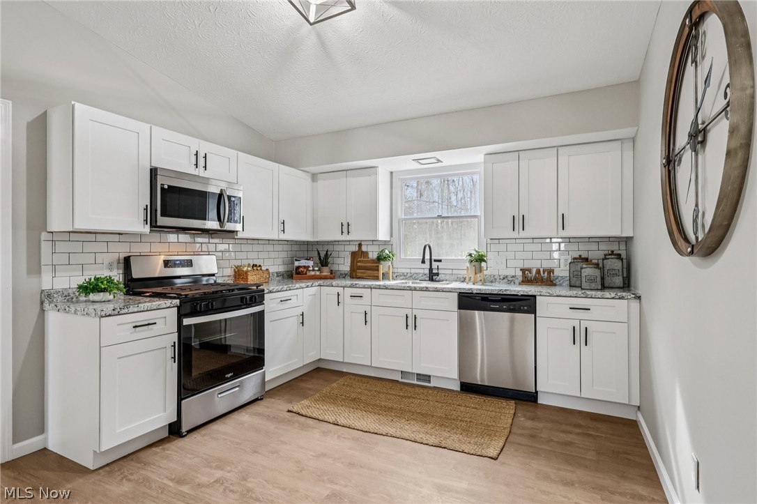 Kitchen featuring stainless steel appliances, white cabinetry, and light stone counters