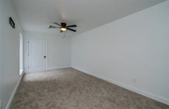 an empty room with a ceiling fan and carpet