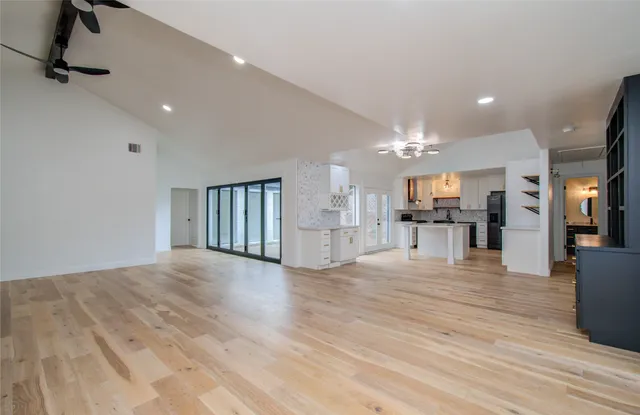 a view of an empty room and kitchen with wooden floor