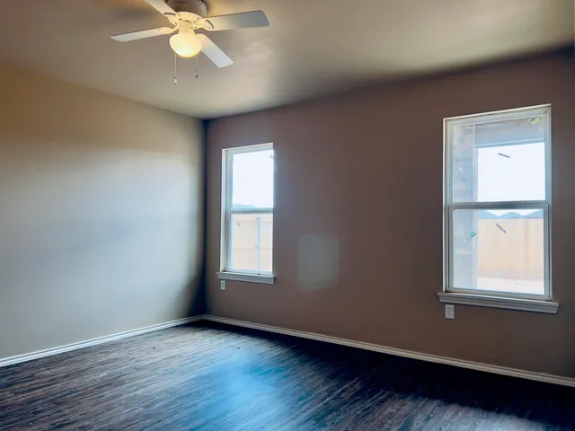 an empty room with wooden floor fan and windows