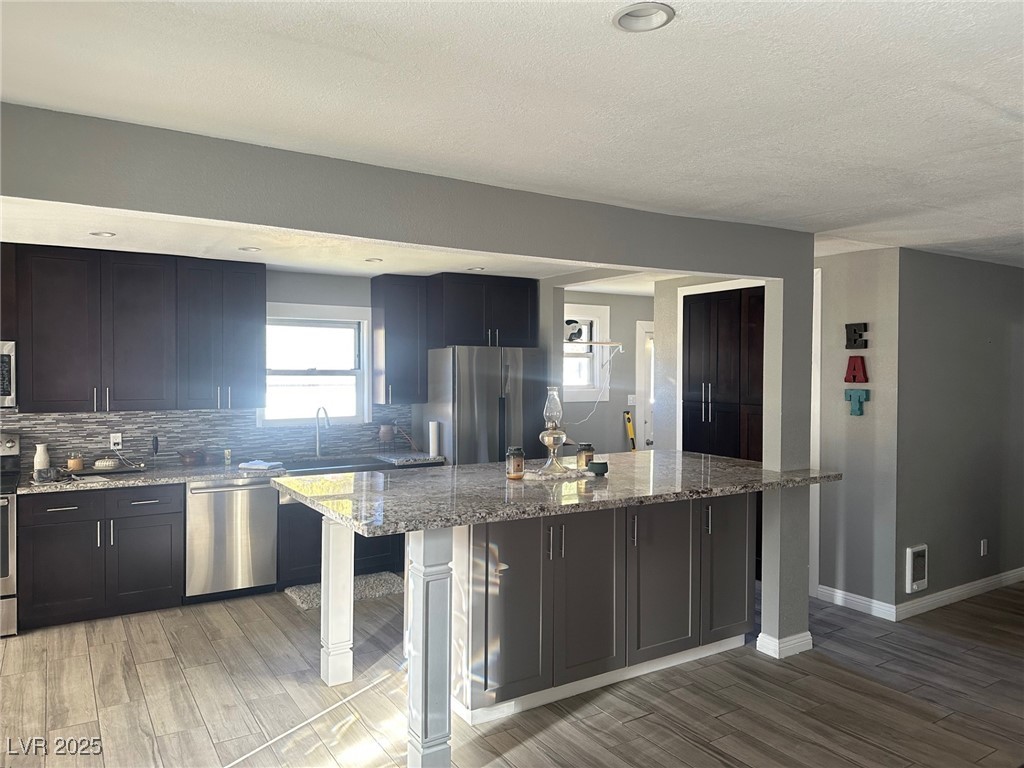 966 Mill Street Ely, NV 89301 - Photo 1 of 14 Kitchen with light stone countertops, light wood-style floors, stainless steel appliances, a center island, and backsplash
