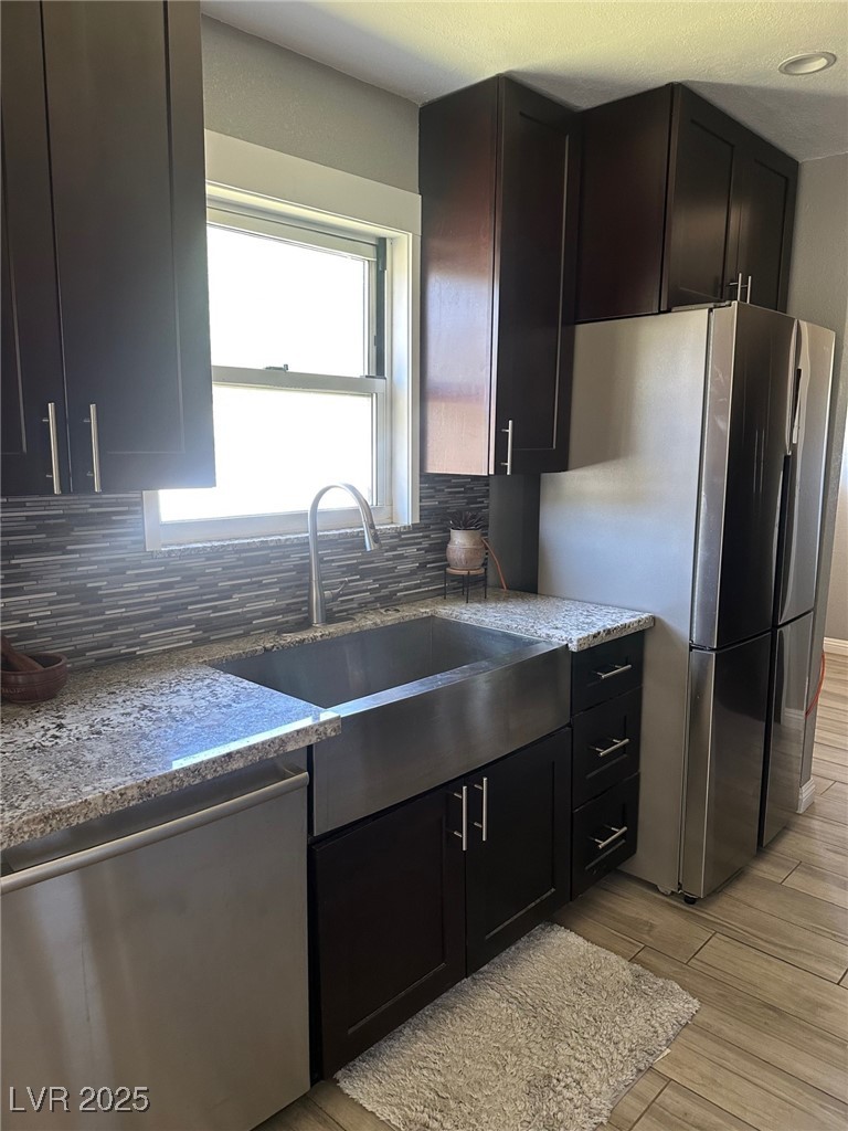 966 Mill Street Ely, NV 89301 - Photo 6 of 14 Kitchen featuring stainless steel appliances, decorative backsplash, light stone countertops, light wood-style flooring, and dark cabinets