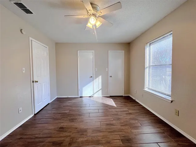 an empty room with wooden floor fan and windows