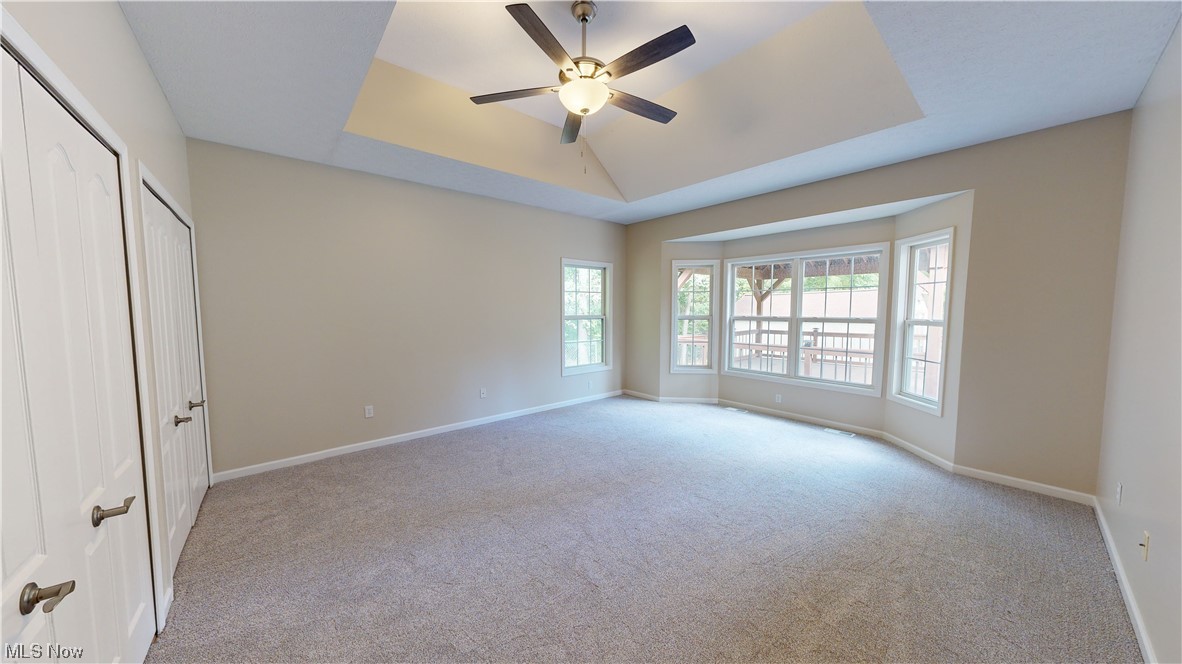 Bedroom with light carpet, ceiling fan, and a raised ceiling