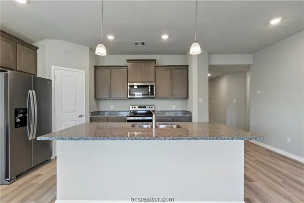 a kitchen with stainless steel appliances granite countertop a refrigerator a sink a stove a microwave and white cabinets with wooden floor