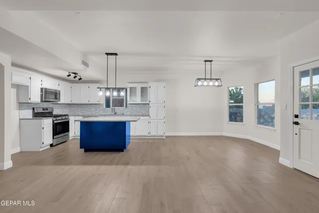 a large kitchen with stainless steel appliances granite countertop a stove a sink dishwasher and white cabinets with wooden floor