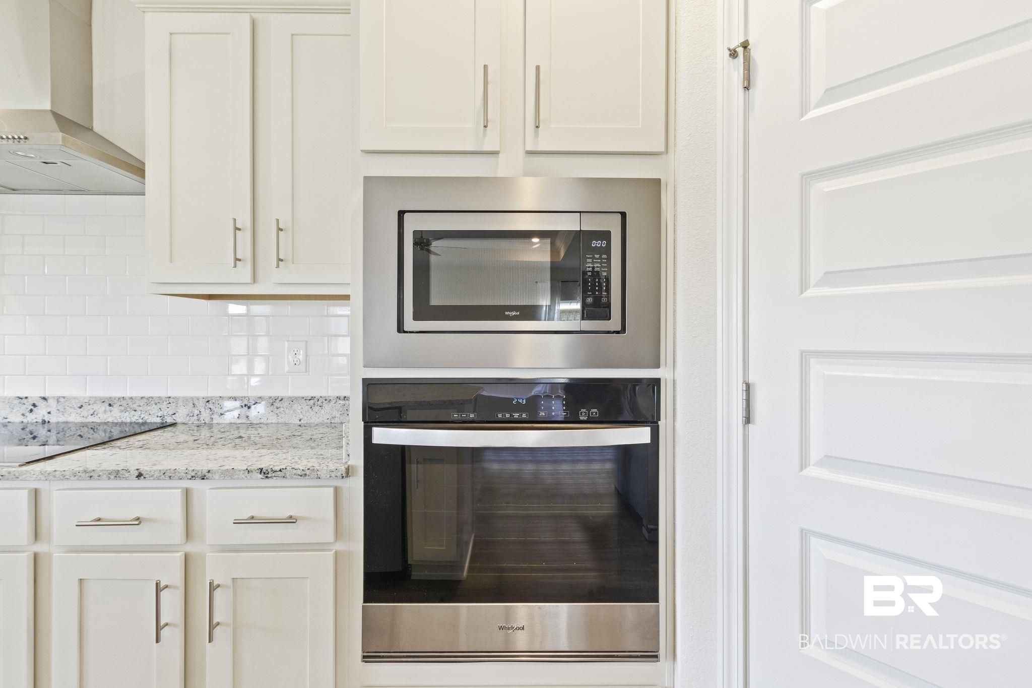 11303 Genuine Risk Circle Daphne, AL 36526 - Photo 30 of 100 Kitchen featuring appliances with stainless steel finishes, wall chimney exhaust hood, decorative backsplash, light stone counters, and white cabinetry